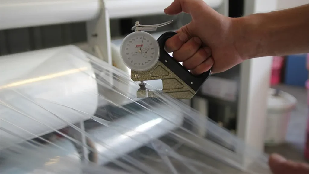 Technician measuring plastic film thickness during quality inspection
